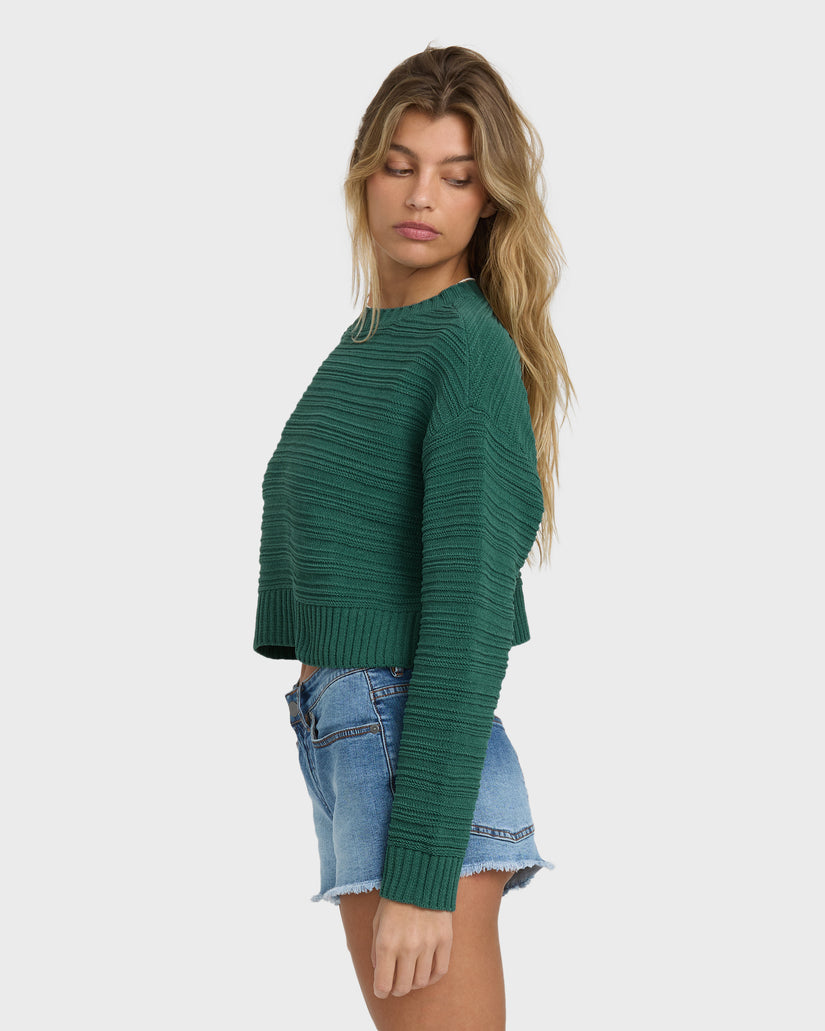 Dark green ribbed knit sweater with crew neckline and long sleeves on model wearing denim shorts.