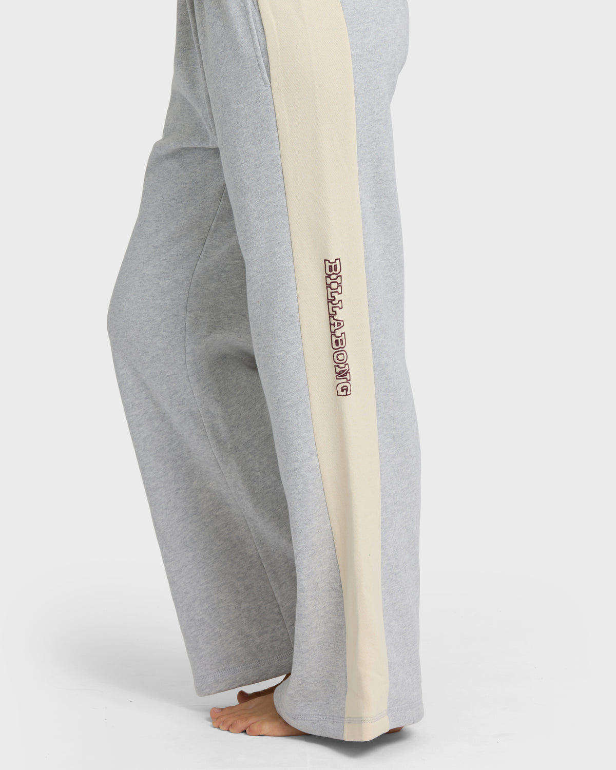 Heather grey sweatpants with cream side stripe and embroidered text on leg, shown on model from waist down.