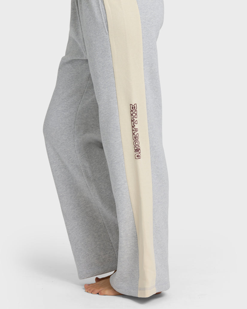 Heather grey sweatpants with cream side stripe and embroidered text on leg, shown on model from waist down.