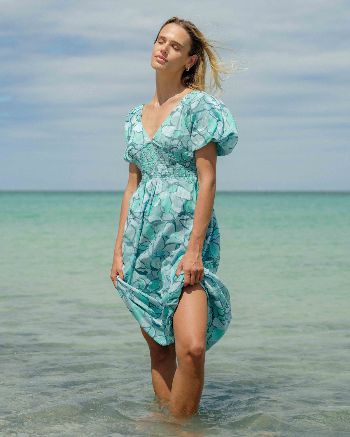 Blue and white leaf-print midi dress with puffed short sleeves and ruched waist detail worn in shallow ocean water.
