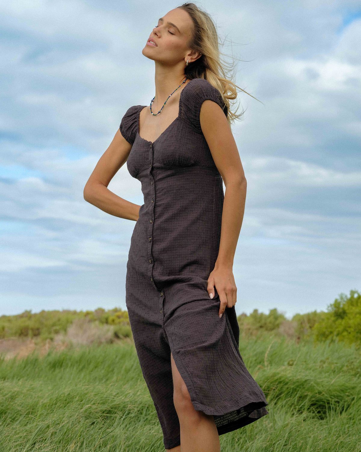 Woman wearing a charcoal gray textured midi dress with puffed short sleeves and front button closure.