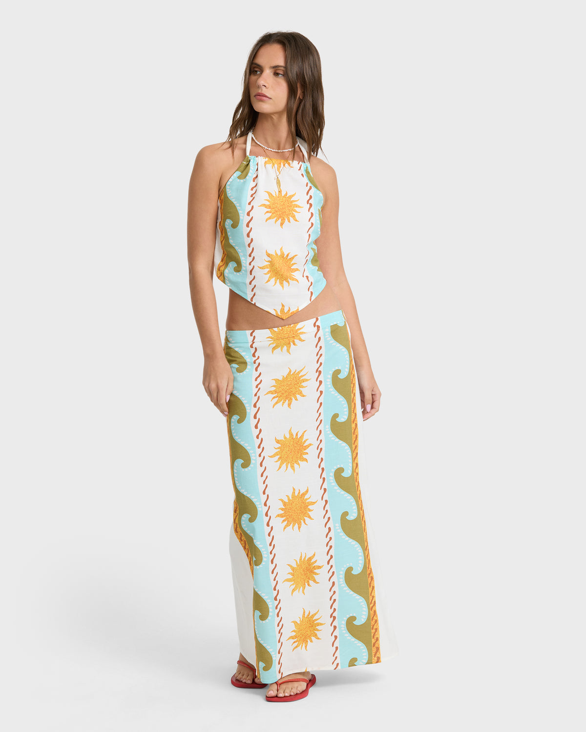 White midi skirt with yellow suns, blue waves, and gold curved patterns, worn with matching cropped halter top.
