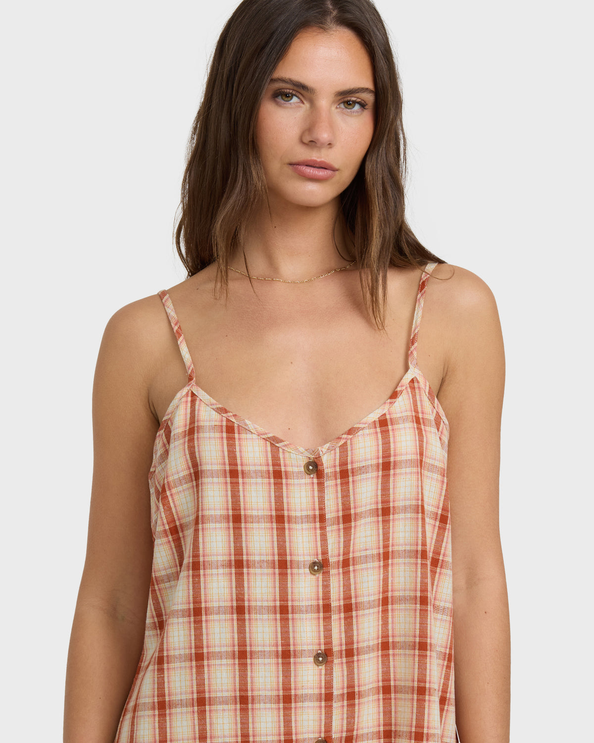 Woman wearing a rust and cream plaid romper with button front and thin straps.