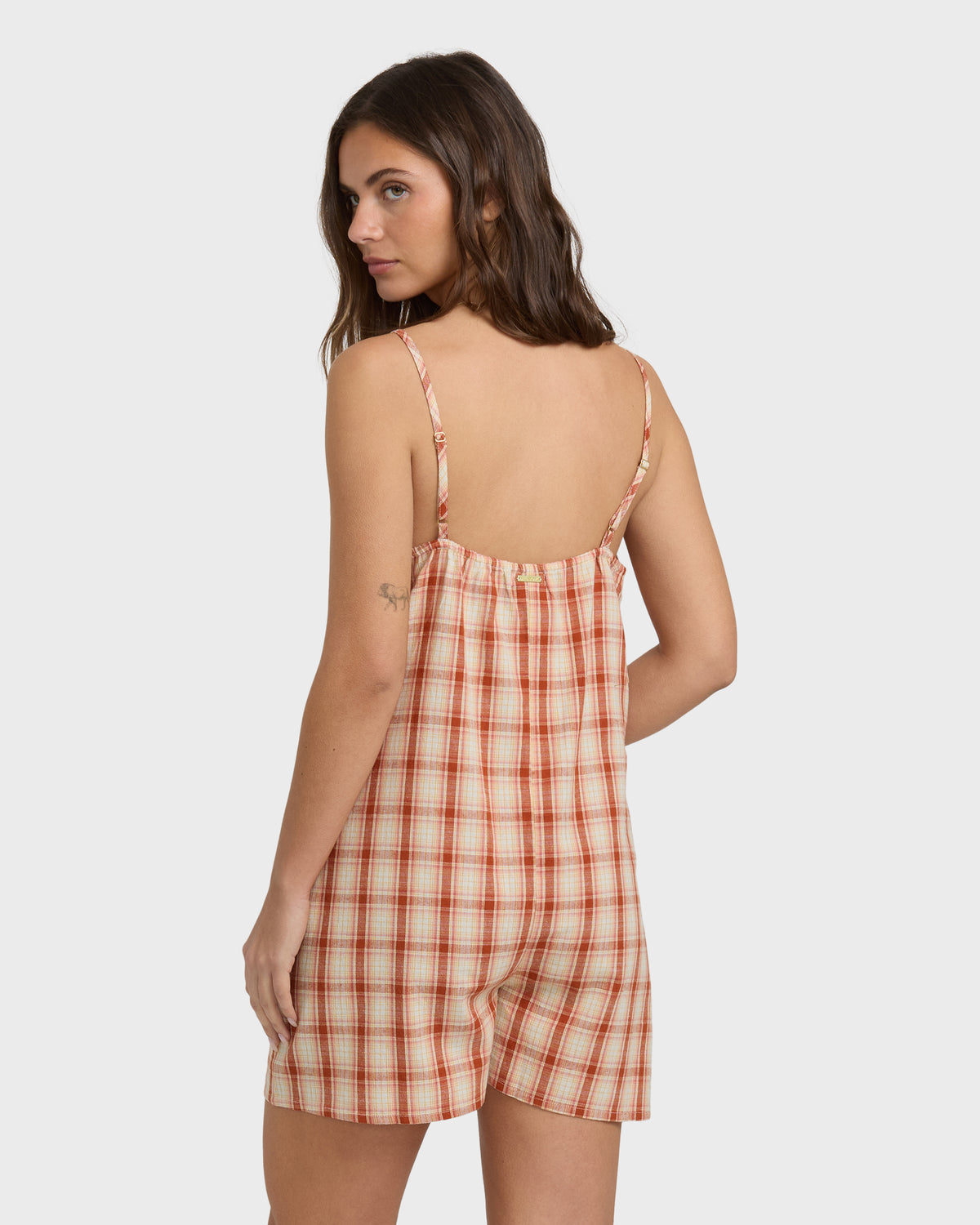 Woman wearing a rust and cream plaid sleeveless romper with thin shoulder straps and open back.