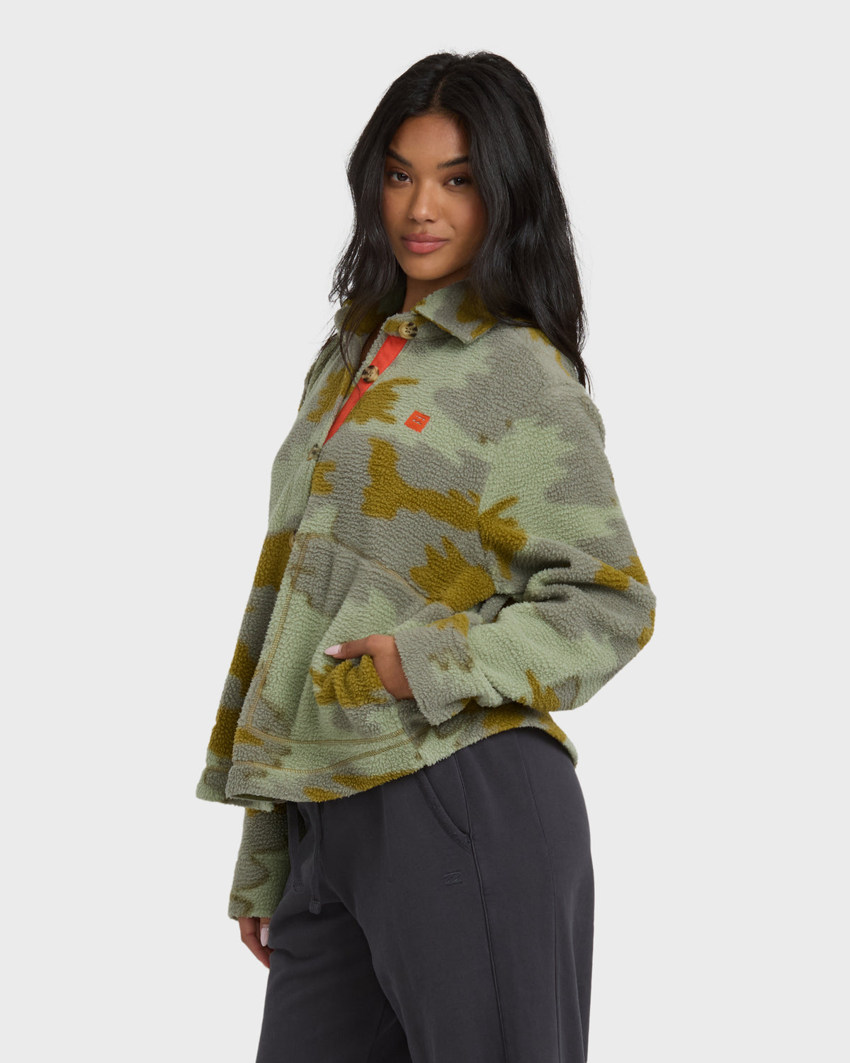 Camouflage sherpa shacket in sage and gold tones with button front and collar, paired with black pants.