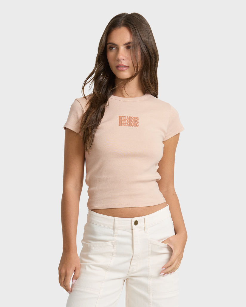 Oatmeal short sleeve t-shirt with small stacked text graphic on chest, worn with white pants.
