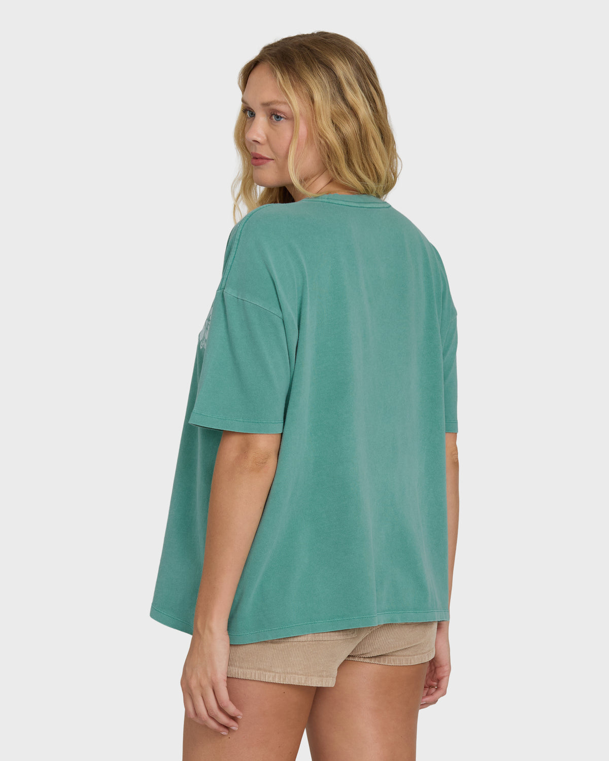 Green short sleeve t-shirt on model shown from back, paired with beige shorts.
