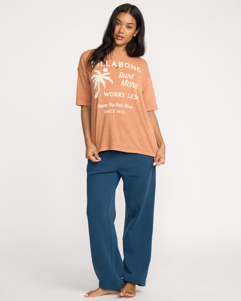 Sunburnt short-sleeve tee with white text and palm tree graphic on front, paired with blue pants.