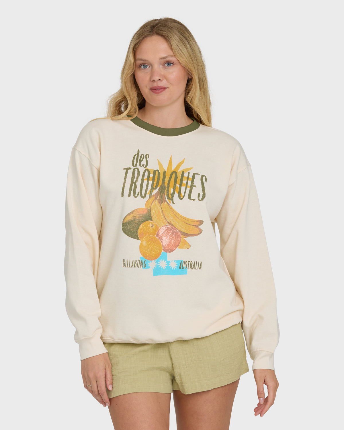 Cream crewneck sweatshirt with tropical fruit graphic and "des Tropiques" text, worn with olive green shorts.