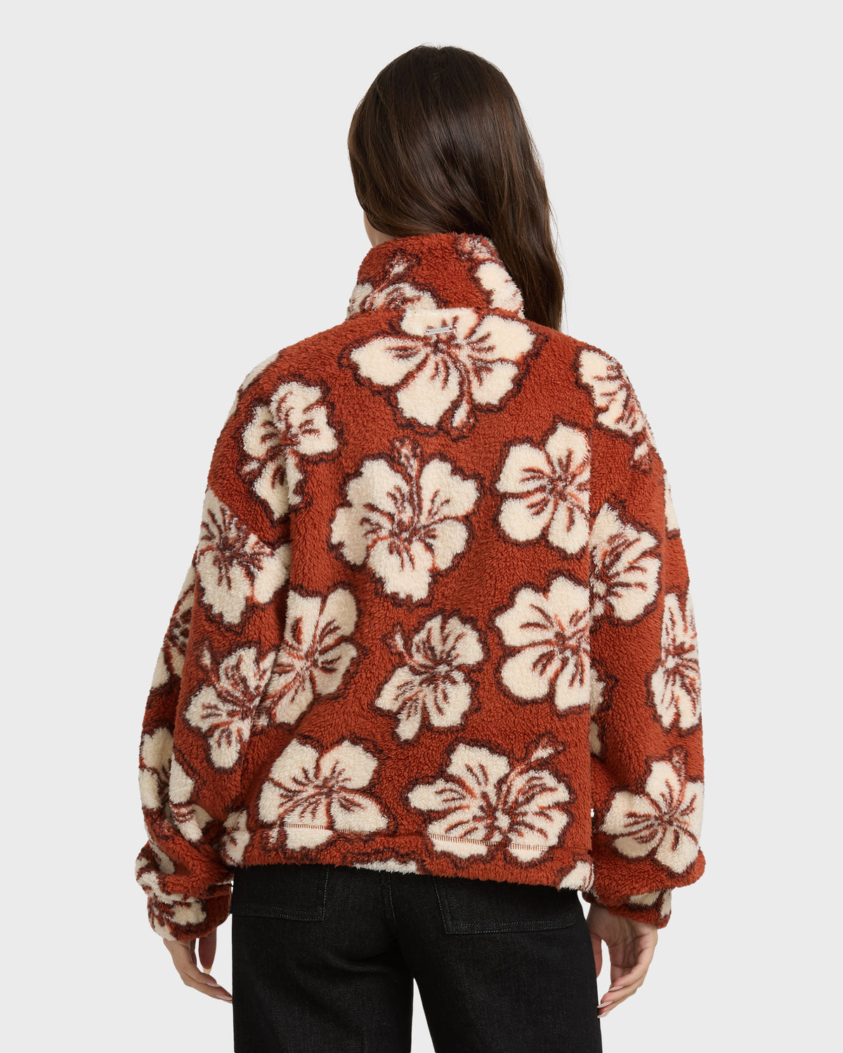 Rust-colored sherpa half zip sweatshirt with cream floral pattern, shown from back on model wearing black pants.