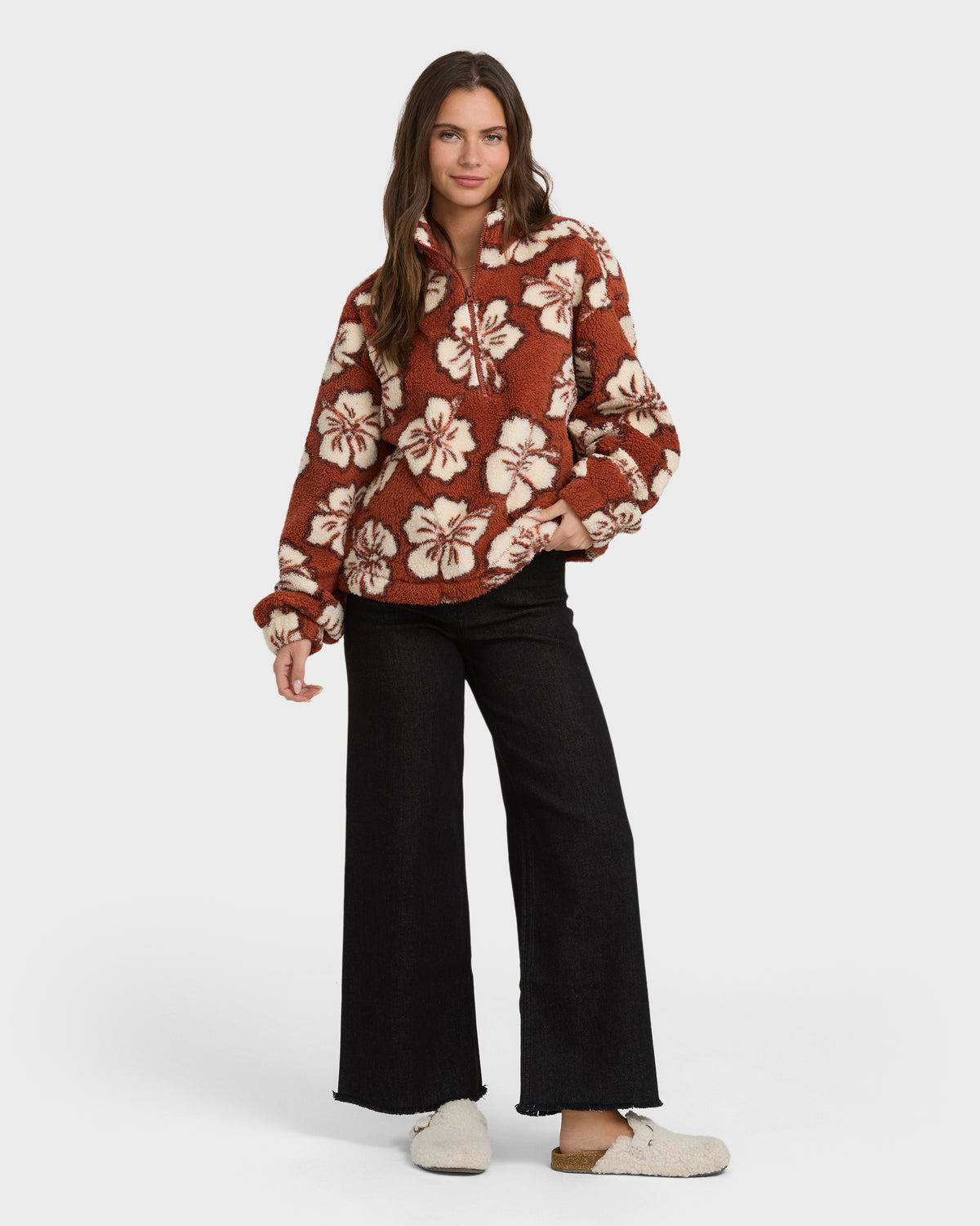 Rust-colored sherpa half-zip sweatshirt with cream floral pattern, styled with black wide-leg jeans.
