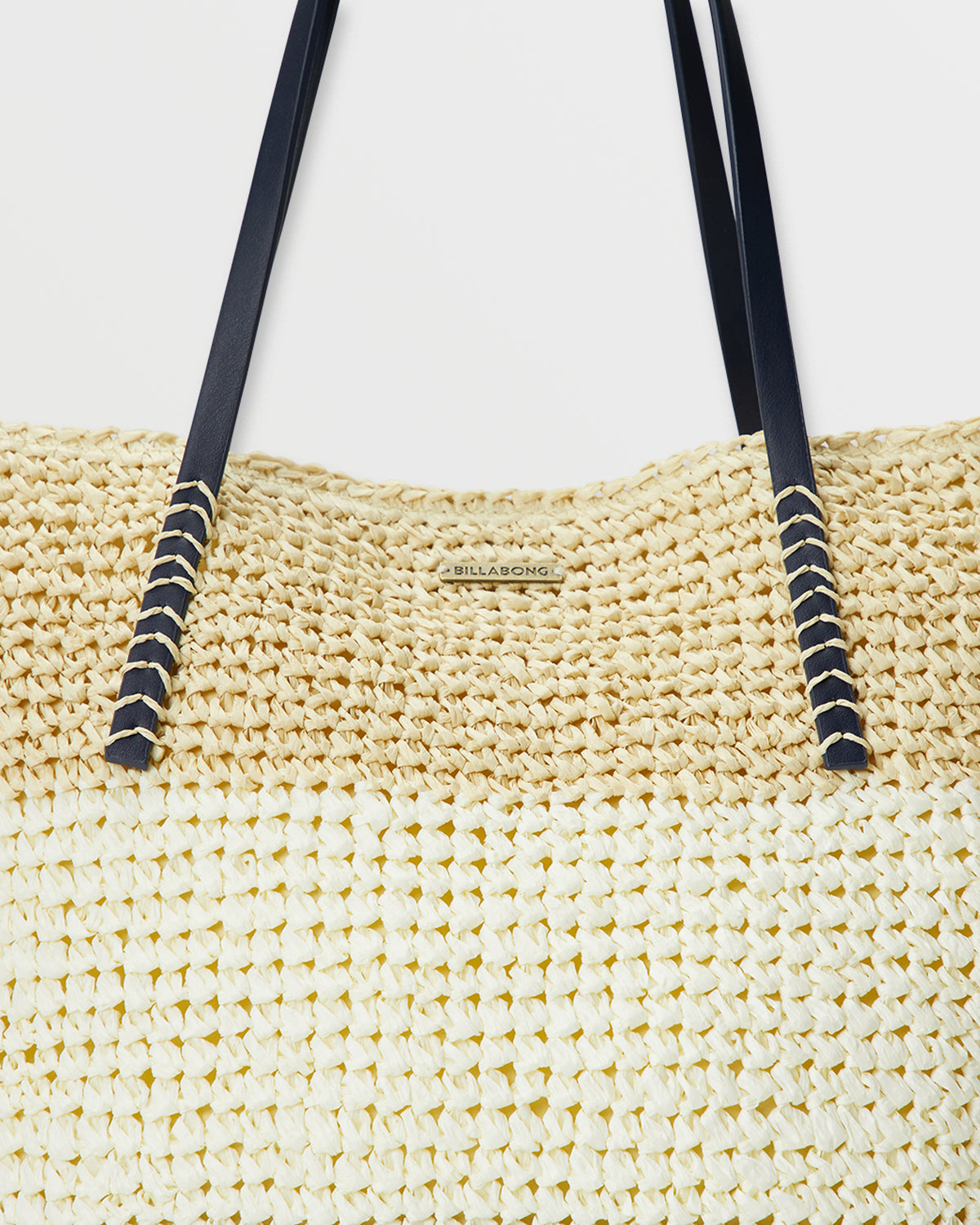 Woven straw tote bag in cream with navy shoulder straps and decorative rope detailing.