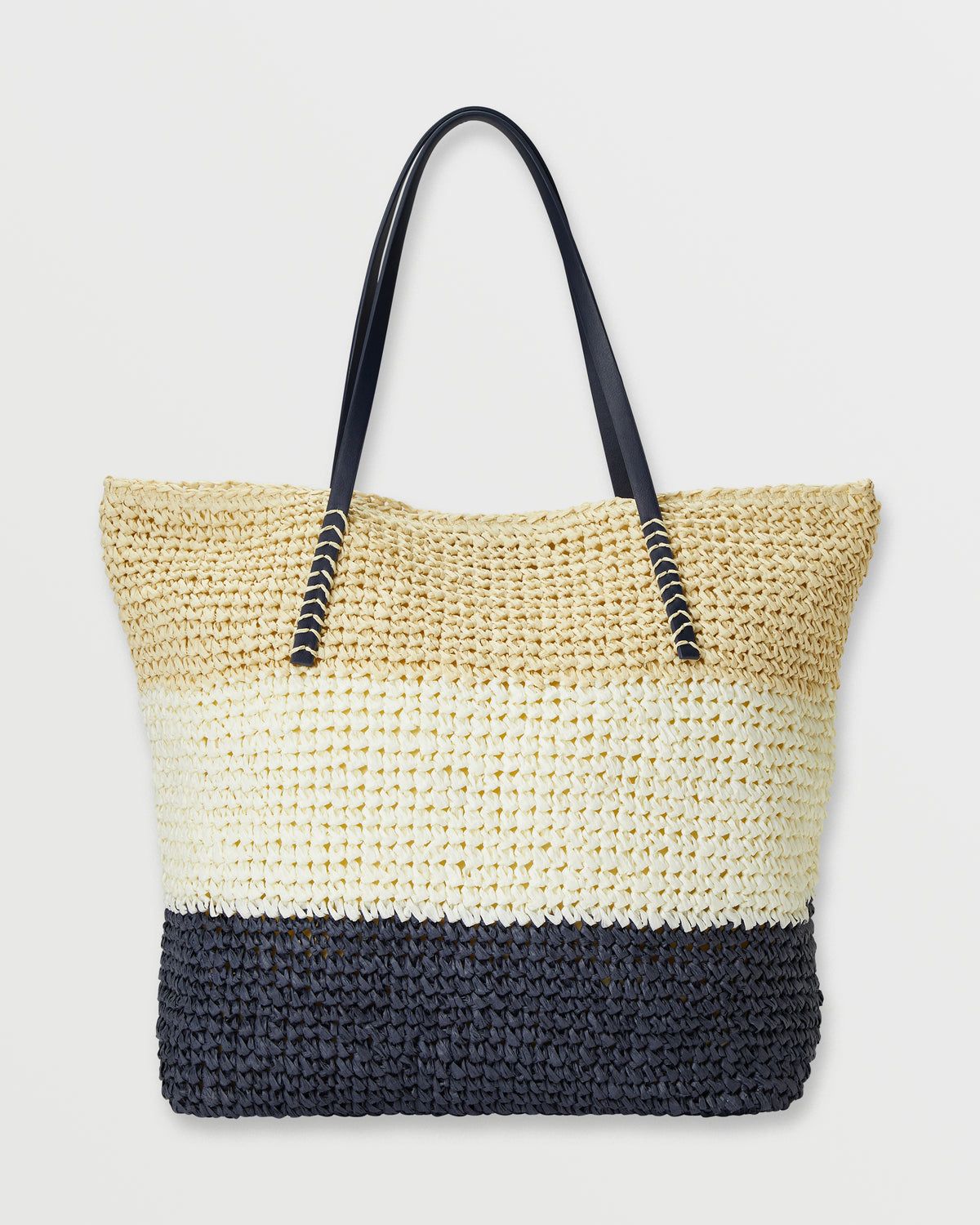 Woven straw tote bag with color-blocked design in natural, cream, and black sections, featuring black handles with metallic a