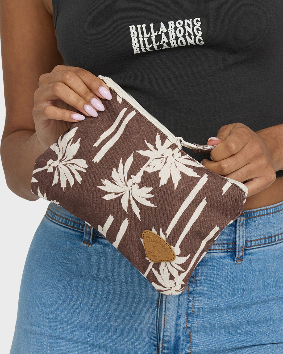 Nutmeg zip pouch with white palm leaf and stripe pattern, tan leather patch detail, held in hands.