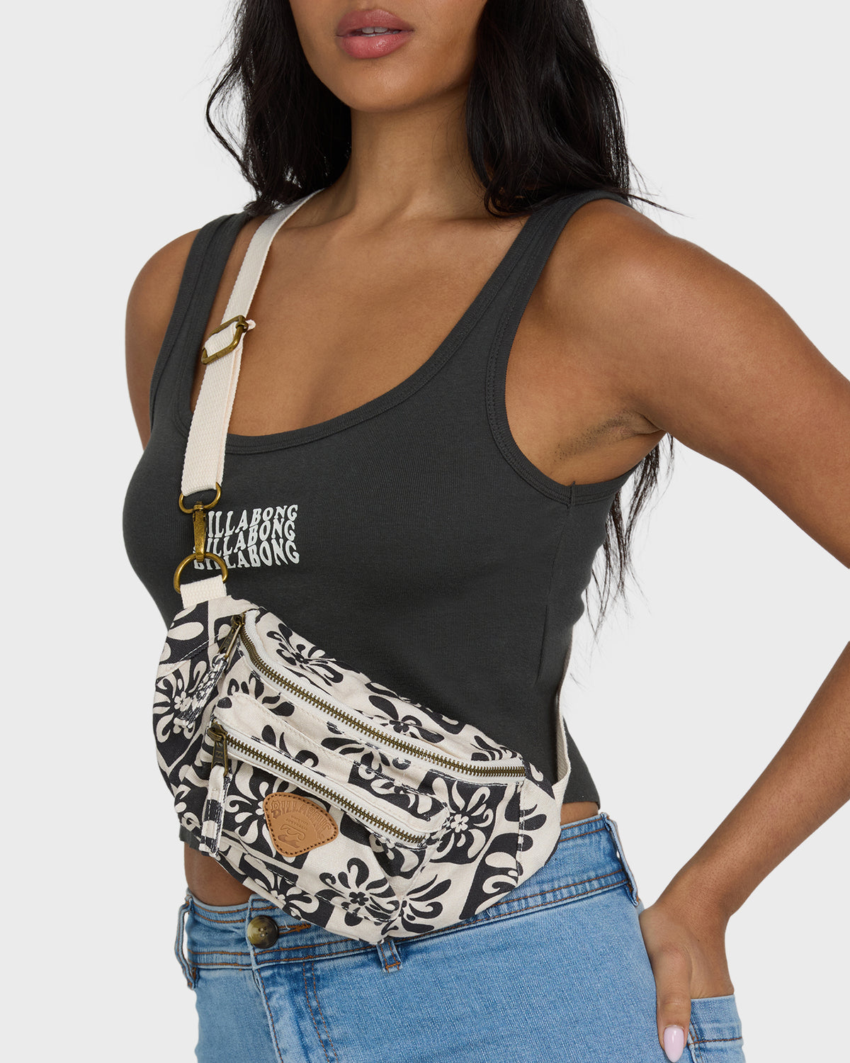 Black and cream patterned waistbag with multiple zippered compartments and tan leather accent, worn across body with beige st