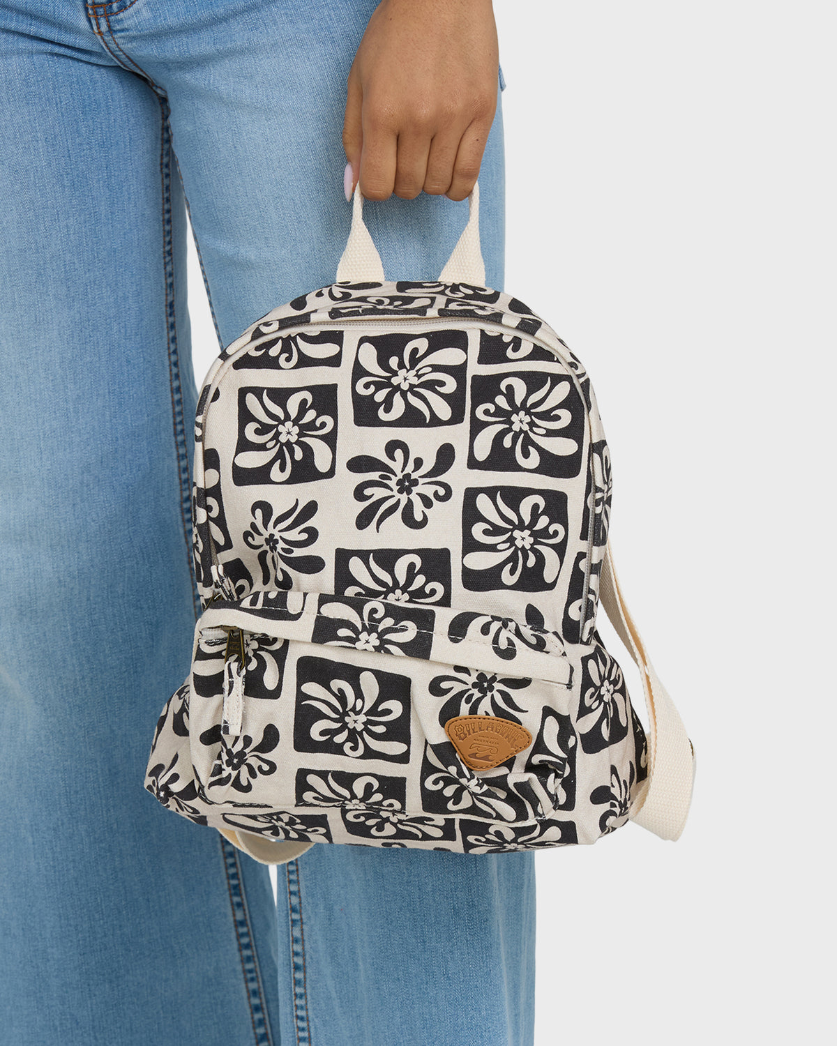 Small backpack with cream and black floral tile pattern, cream handles, and brown leather accent patch.