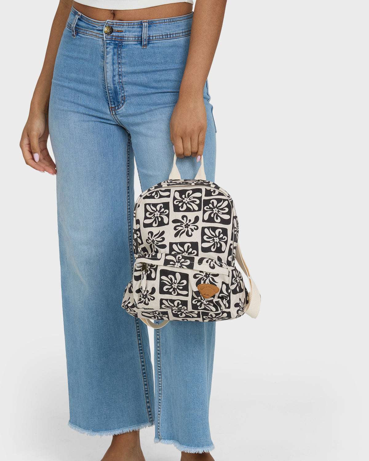 Black and white floral patterned mini backpack with tan leather accent held by person in blue jeans.
