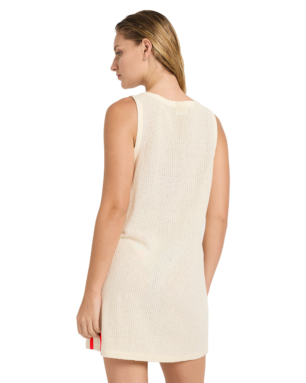 Woman wearing a sleeveless cream-colored textured knit dress with a red and white striped detail at the hem, shown from the b