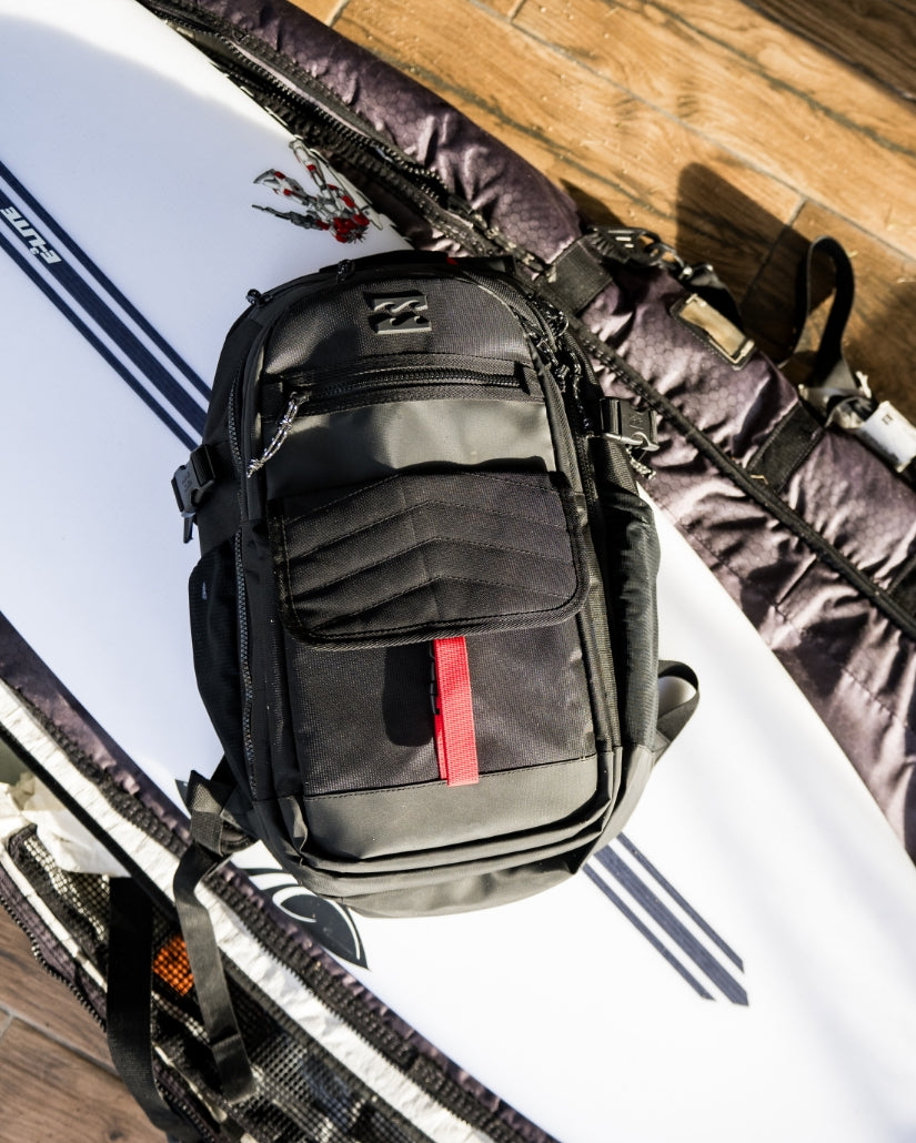 Black backpack with gray panels, multiple compartments, red stripe detail, and padded shoulder straps displayed on wooden sur