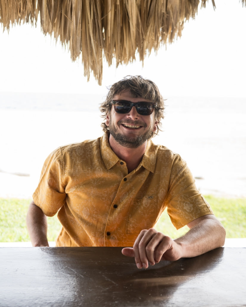 Golden tan jacquard short sleeve button-up shirt with subtle textured pattern worn by man at outdoor table.