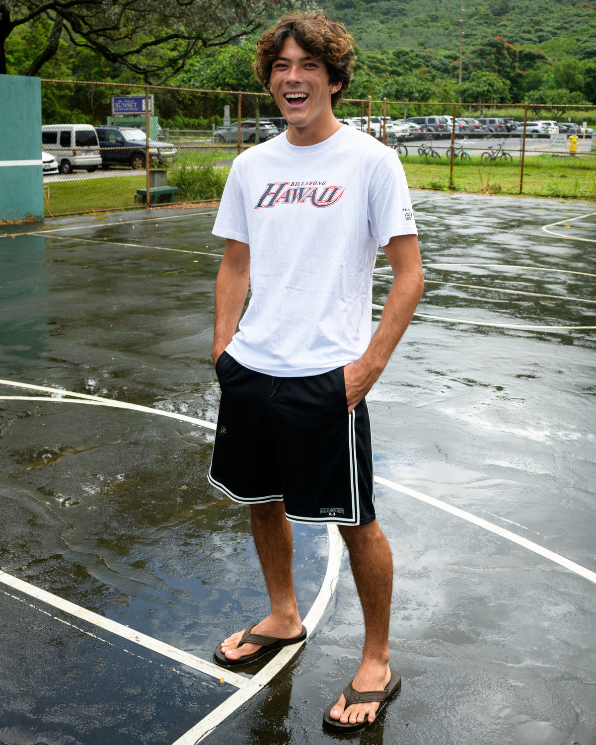 Man wearing white short sleeve t-shirt with graphic print on wet tennis court.