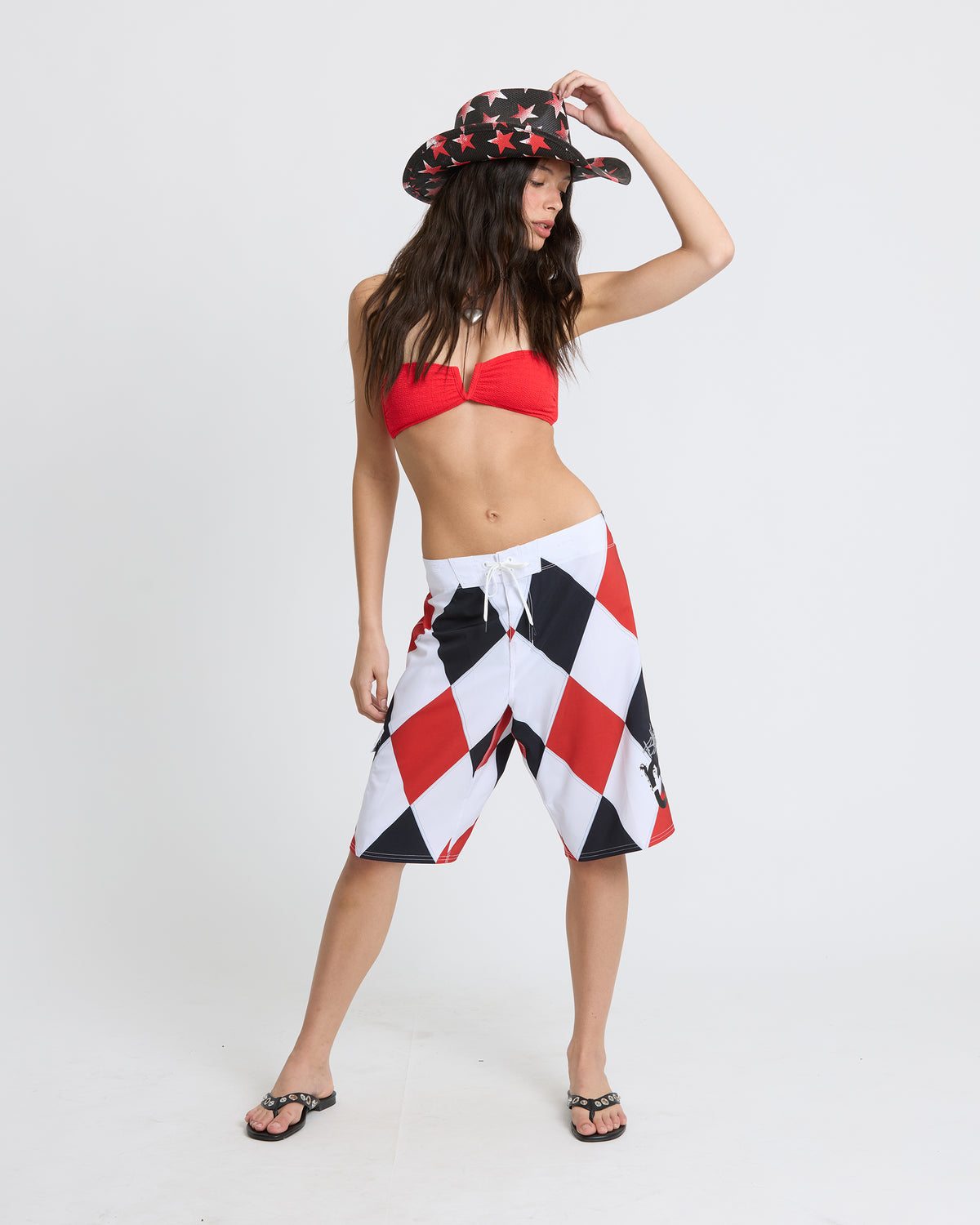 Woman wearing black and red star-patterned bucket hat, red bikini top, and red/white/black diamond-patterned shorts.