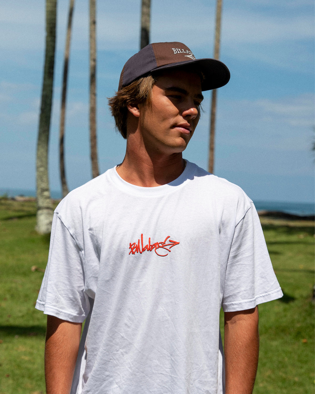White short sleeve cotton t-shirt with red script logo on chest, shown on male model outdoors.