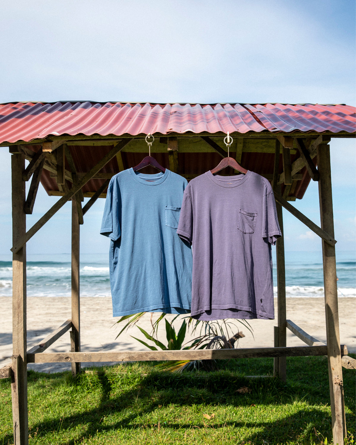 Grey violet crew neck t-shirt with chest pocket, displayed on hanger next to blue t-shirt.