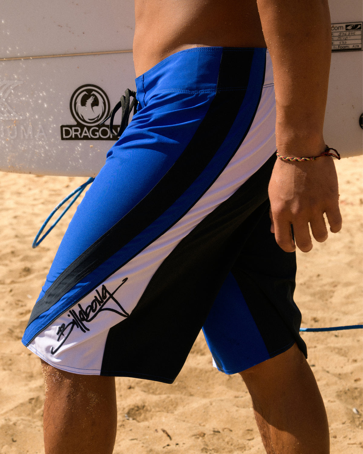 Blue, black, and white boardshorts with color-block design worn on beach.