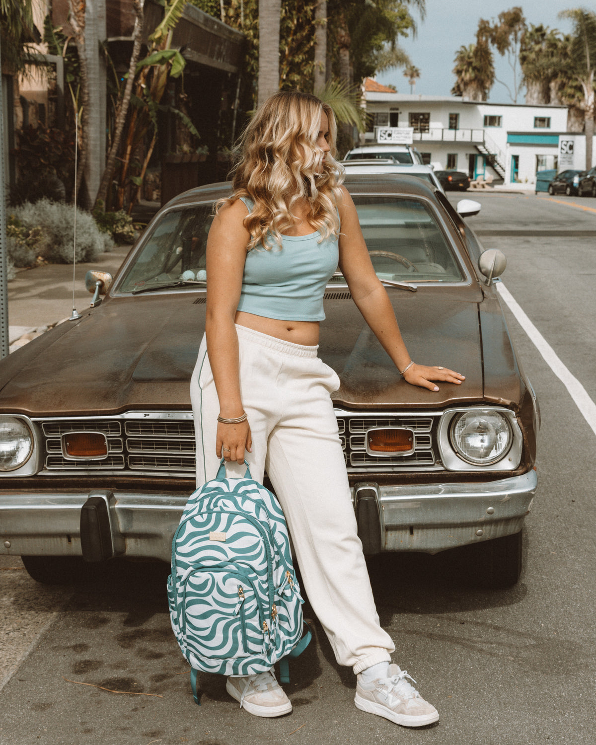 Evergreen backpack with teal and white wavy pattern, held by person standing in front of vintage car.