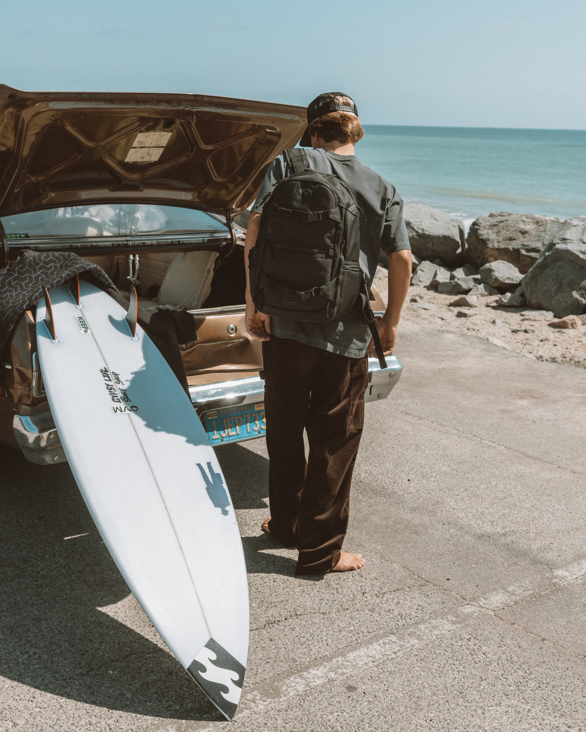 Brown cord pants worn by person at beach with surfboard and open car trunk.