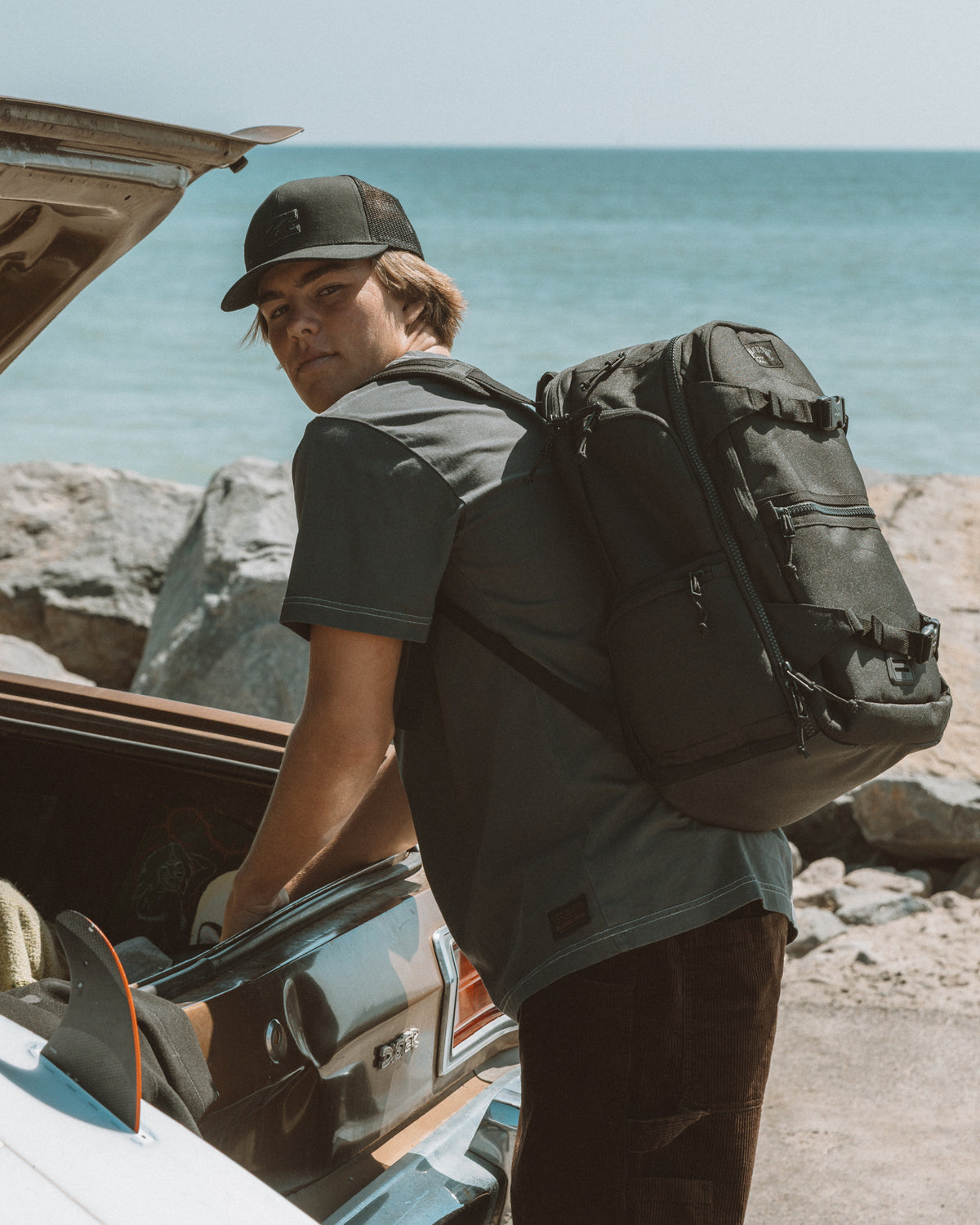 Black 35L backpack worn on person's back at beach, featuring multiple compartments and straps.