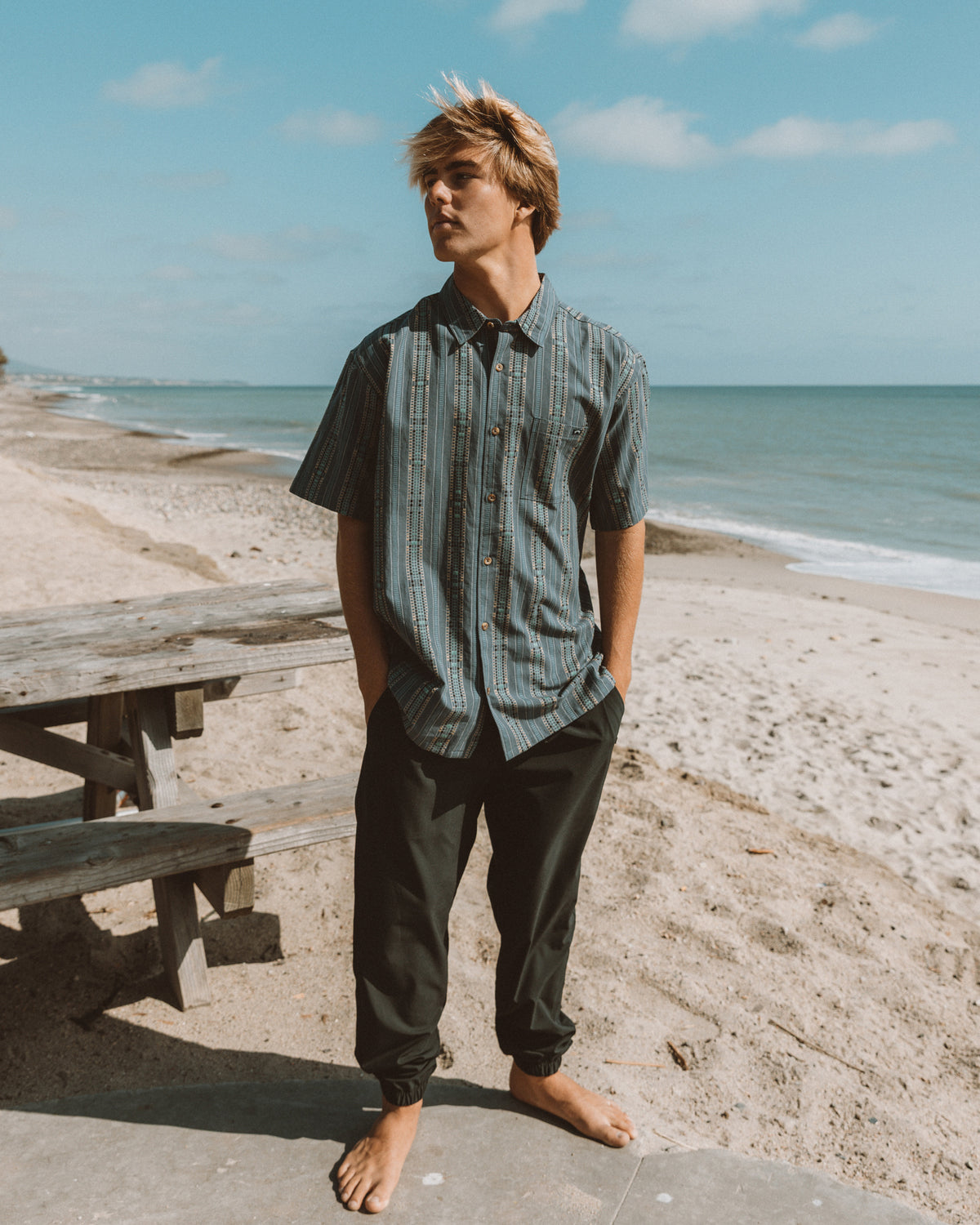 Man wearing black joggers with tapered cuffs and calf-length fit on a beach.