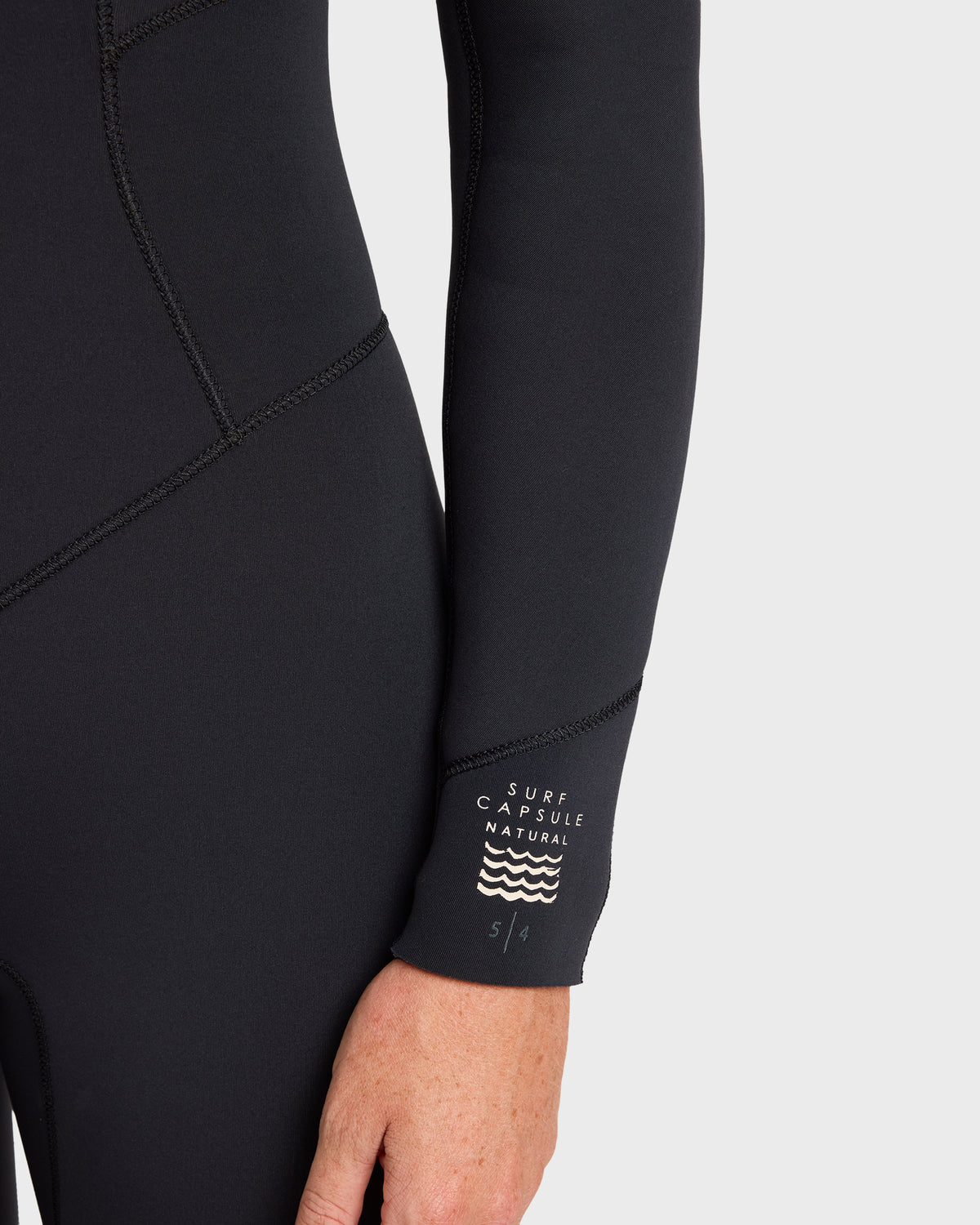 Black full-length wetsuit with chest zip, flat-seam stitching, and "Surf Capsule Natural" branding on sleeve.