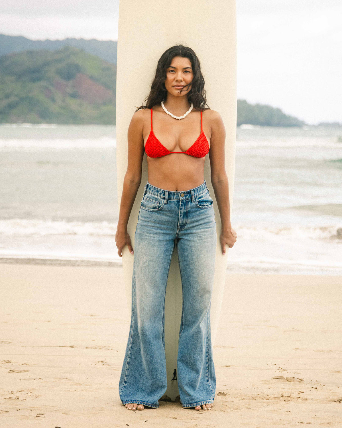 High-waist light blue denim flare pants with distressed details worn on beach.
