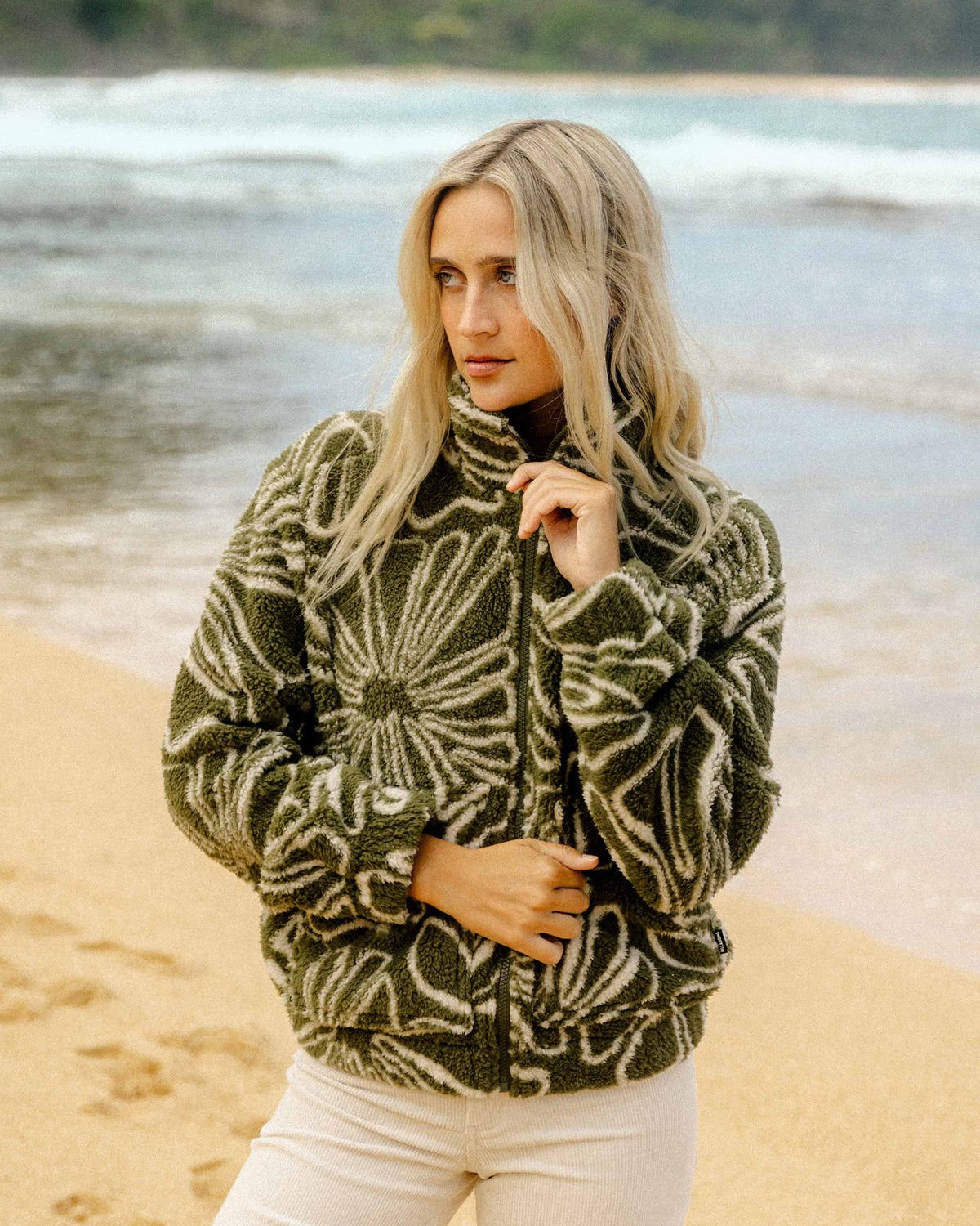 Martini olive sherpa fleece with geometric pattern and front zip, worn on beach with cream pants.