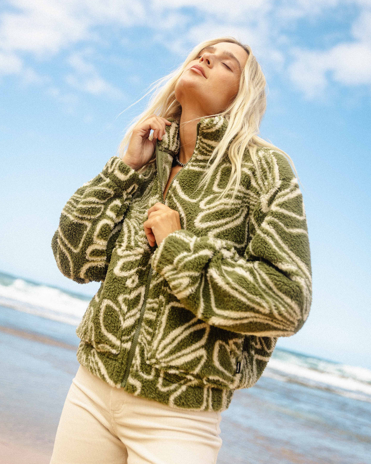 Martini olive sherpa fleece with cream zebra pattern and front zip, worn with cream pants on a beach.