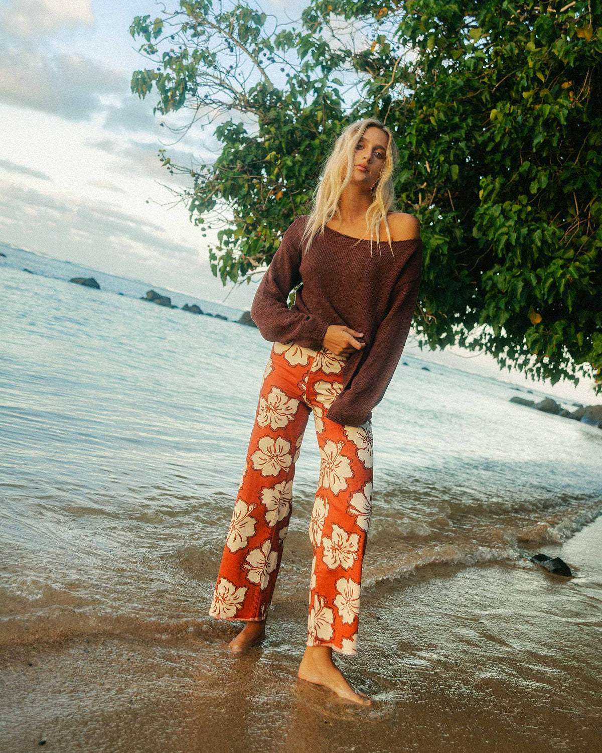 Teak-colored off-shoulder sweater with ribbed knit texture worn with patterned pants at the beach.