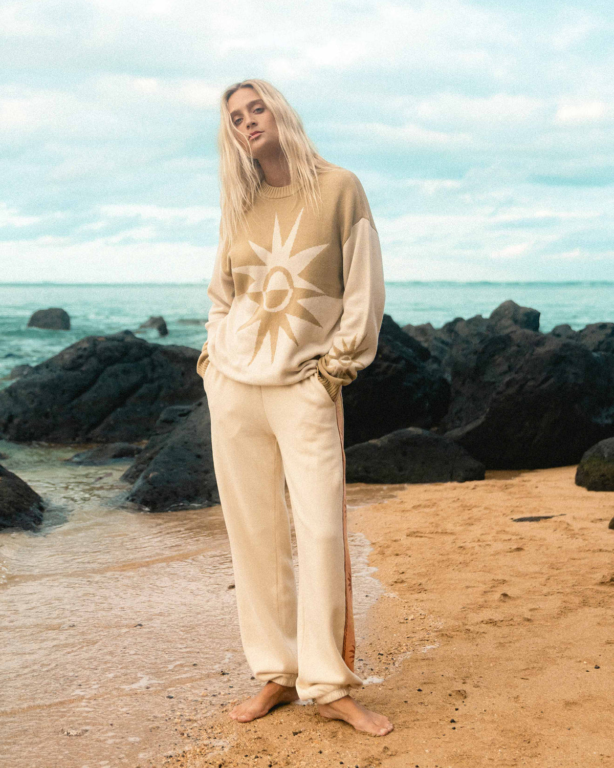 Cream-colored jogger pants with side stripe detail, shown on model at beach.