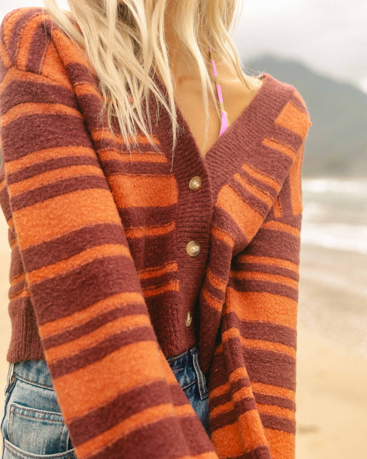 Striped cardigan in burgundy and orange with pearl button front, worn over bikini top at beach.