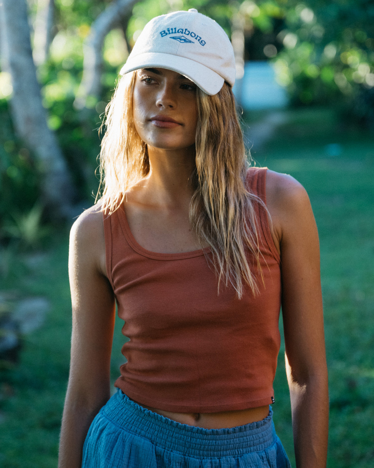 Woman wearing a rust-colored sleeveless knit tank top with a crew neckline and blue skirt.
