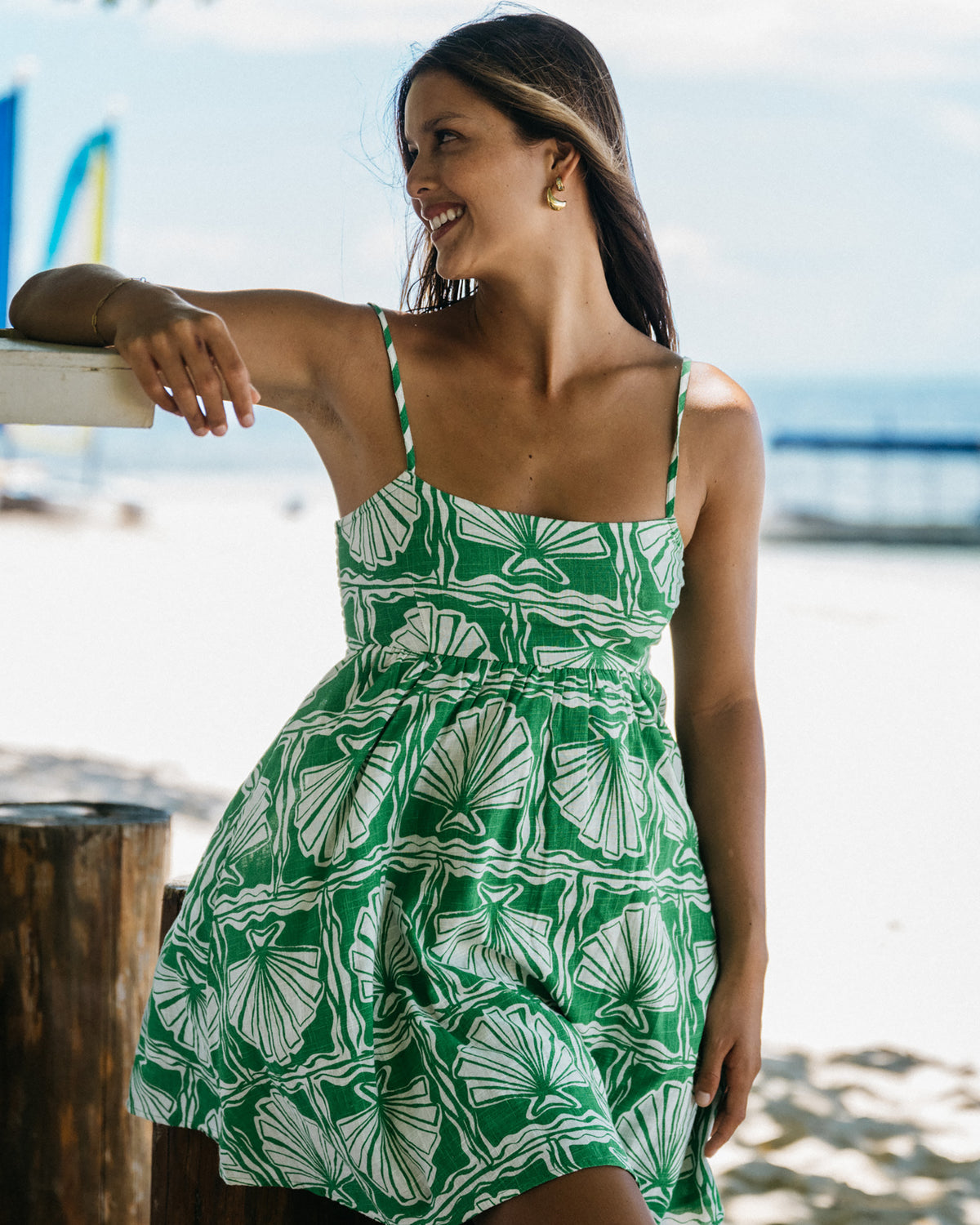 Woman wearing kelly green mini dress with white shell pattern and thin straps at beach.