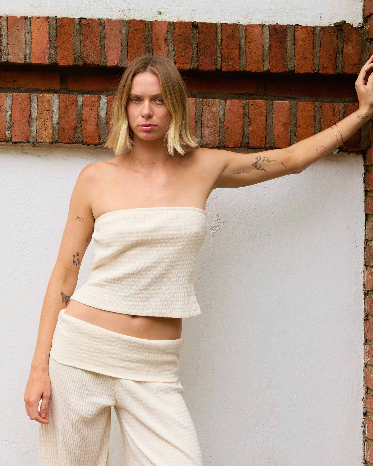 White ribbed tube top with strapless neckline worn by model against brick wall.