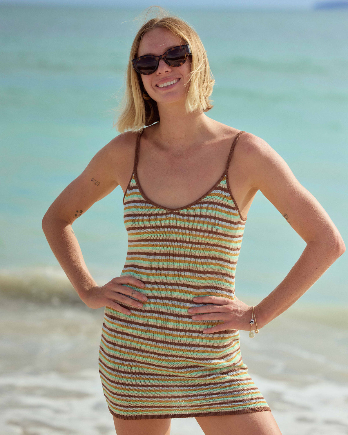 Brown, green, and yellow striped sleeveless mini dress with thin straps worn at the beach.