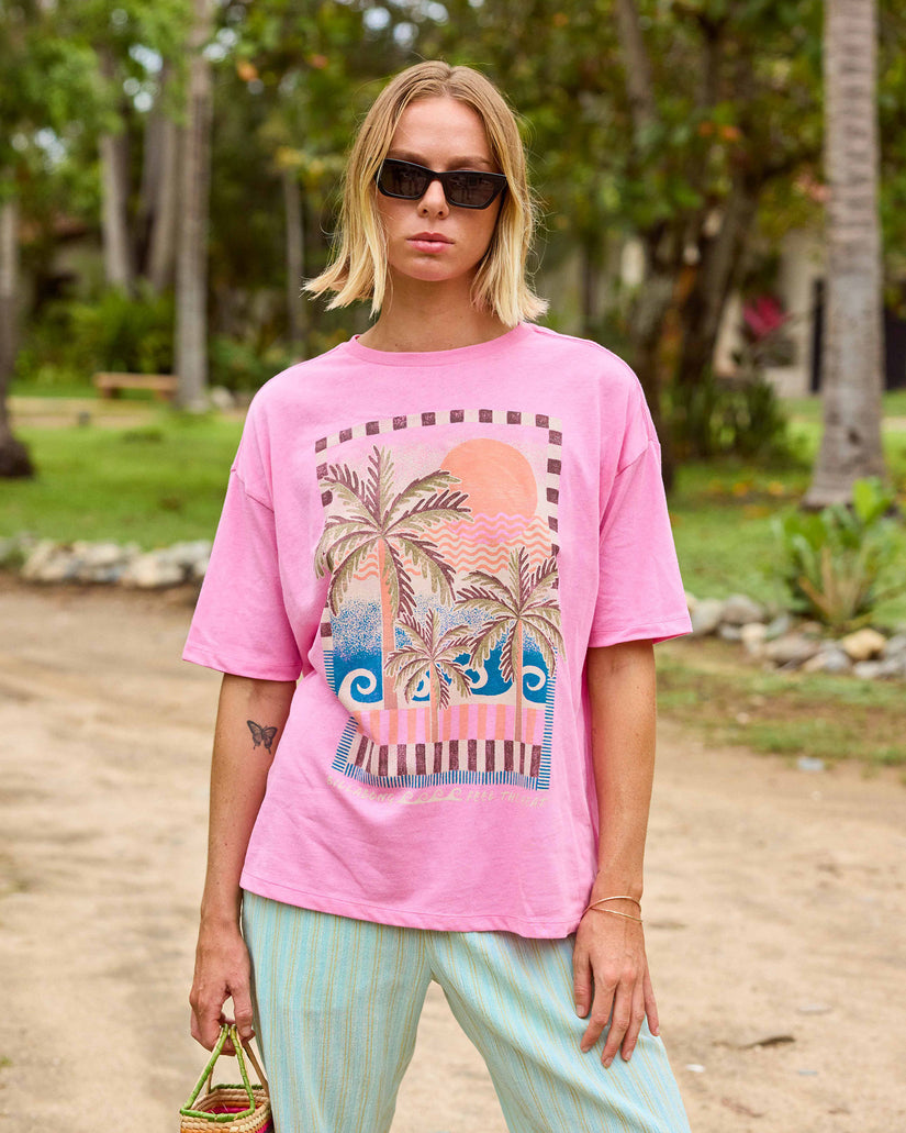 Pink short sleeve knit t-shirt with palm tree and sun graphic print on front.