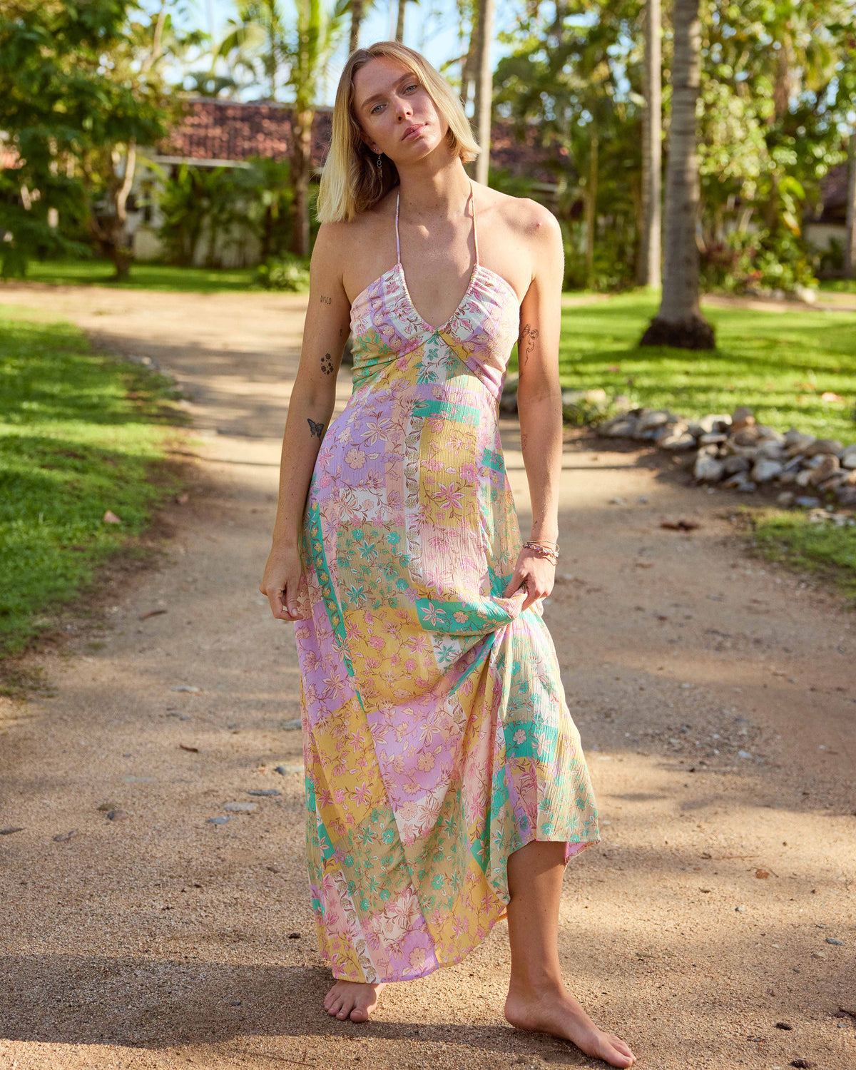 Woman wearing violet maxi dress with colorful floral print, halter neckline, and asymmetrical hem.