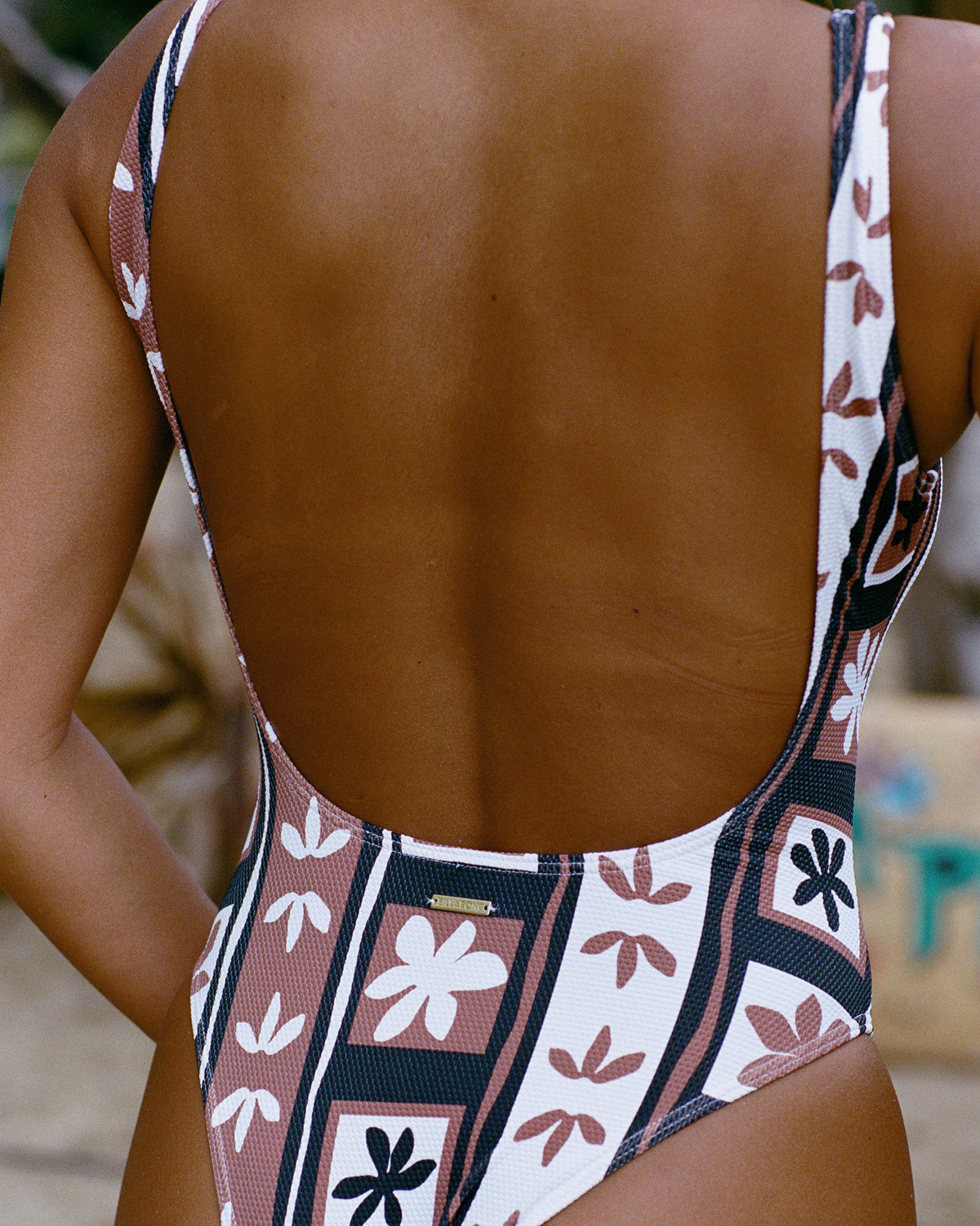 Brown stone one-piece swimsuit with open back and floral patterned straps in cream, brown, and navy colors.