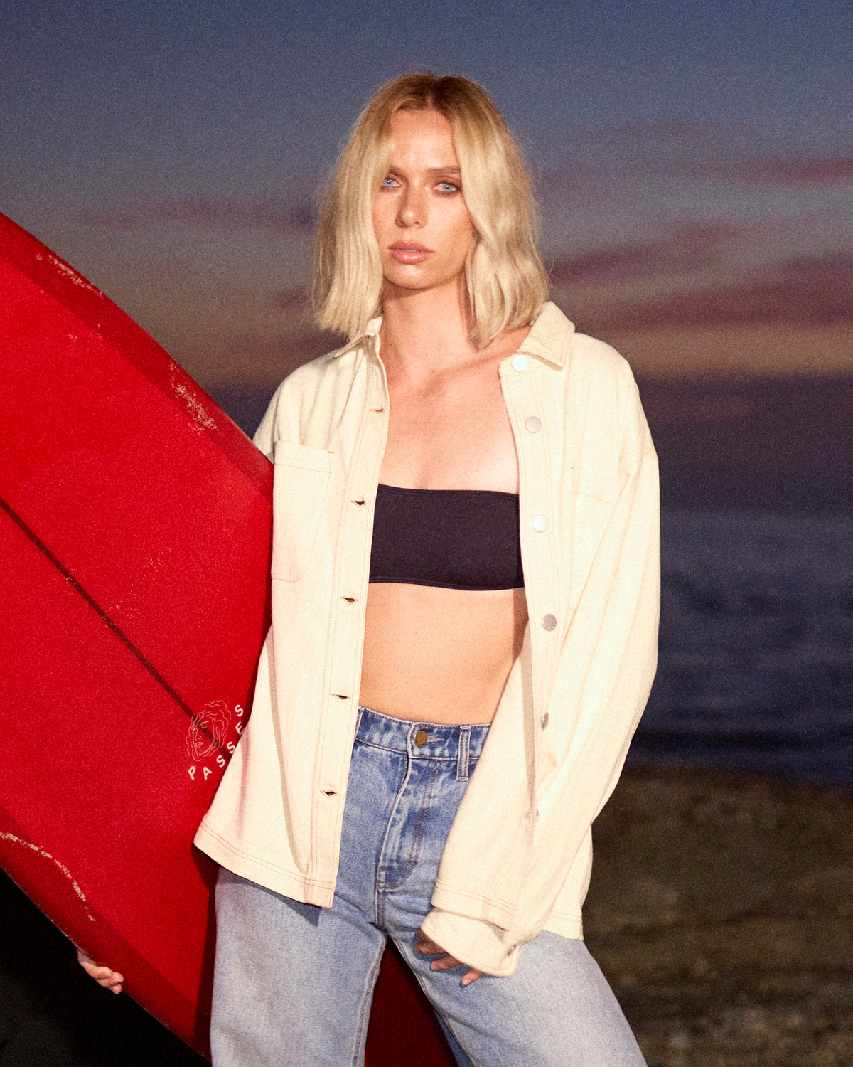 Cream-colored button-up shacket worn open over a black crop top and distressed blue jeans.
