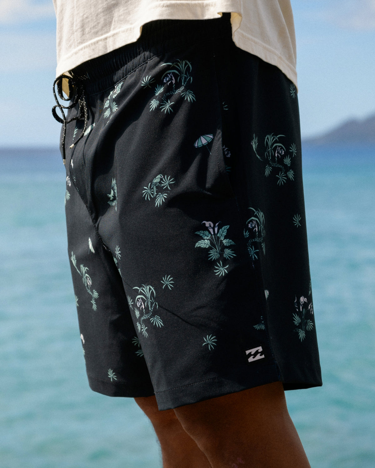 Black swim trunks with multi-colored floral and palm tree pattern, drawstring waist, and side pockets.