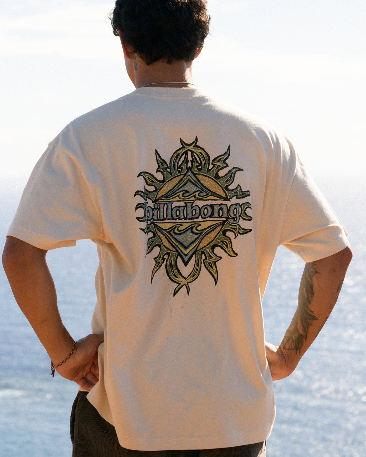 Oatmeal t-shirt with black and gold tribal-style graphic on back featuring "Billabong" text.
